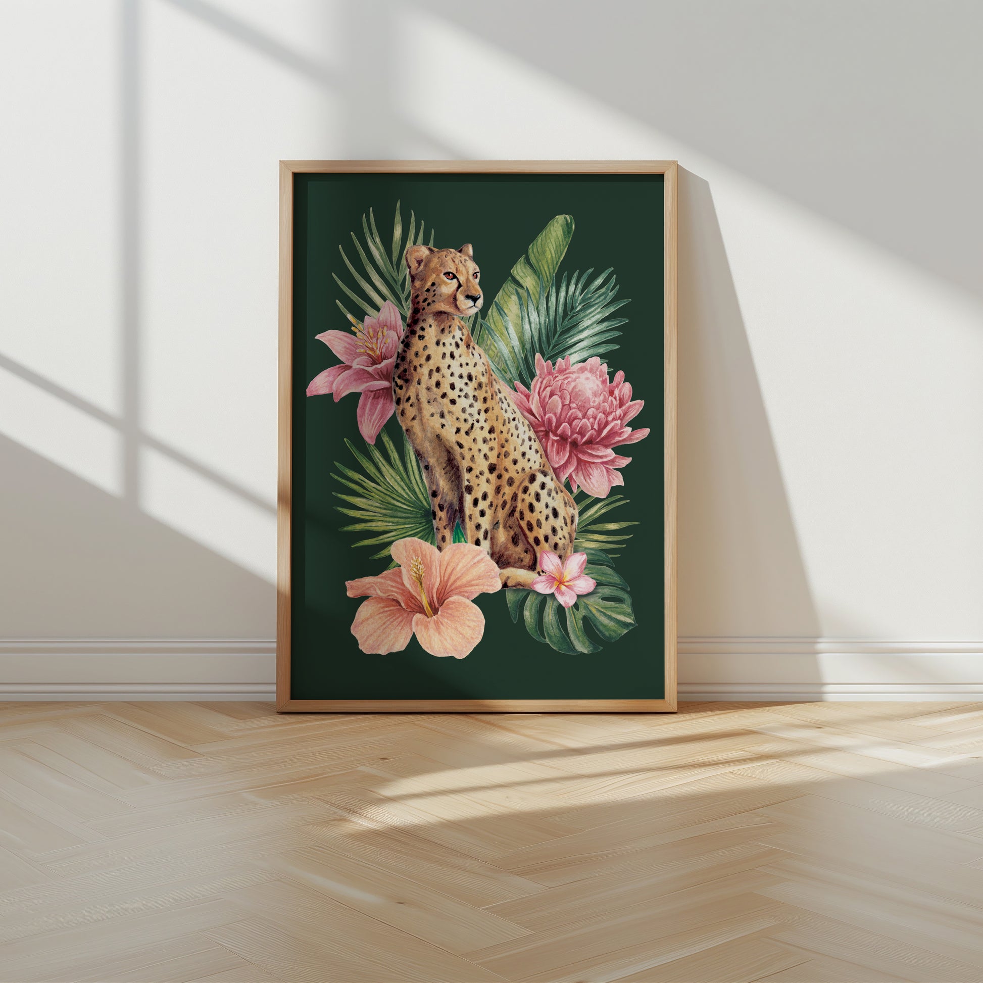 Framed artwork of a cheetah among tropical flowers on a green background, placed on a wooden floor with sunlight casting shadows.