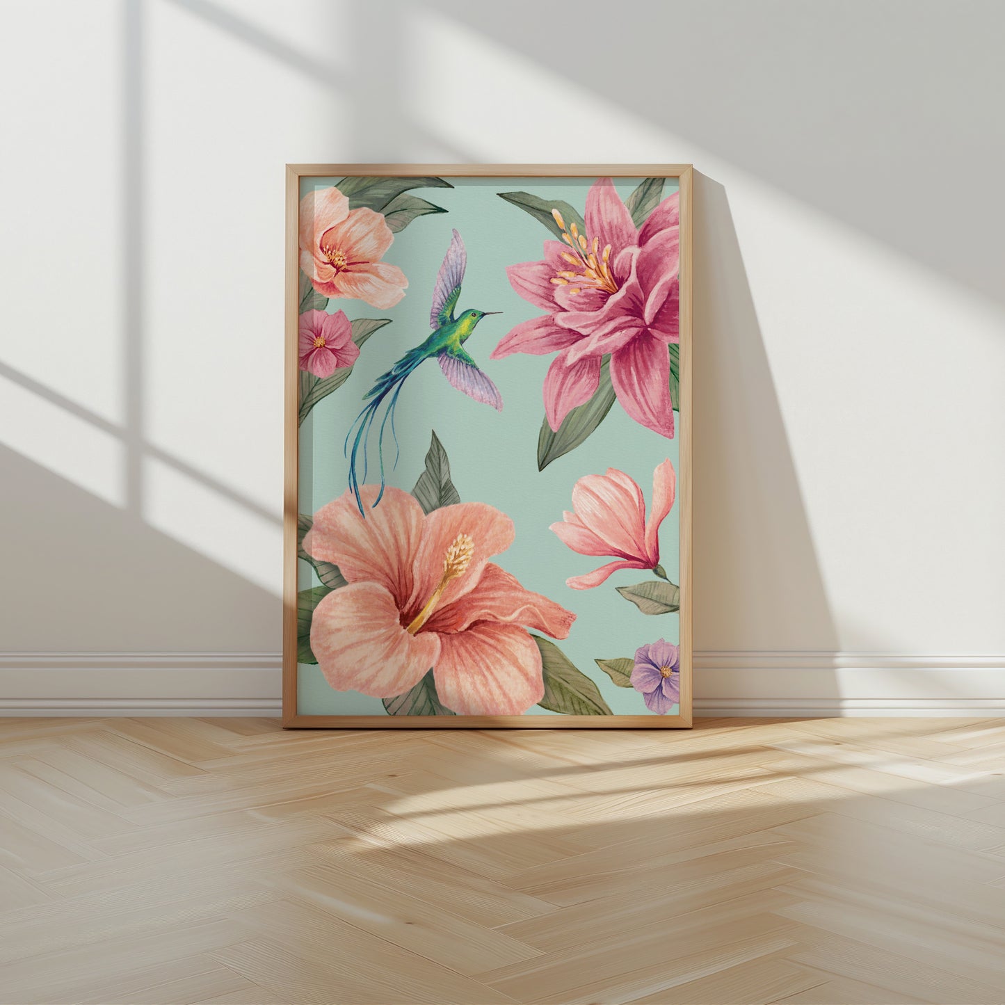 Framed floral artwork with pink flowers and a hummingbird on an aqua blue background, placed on a wooden floor.