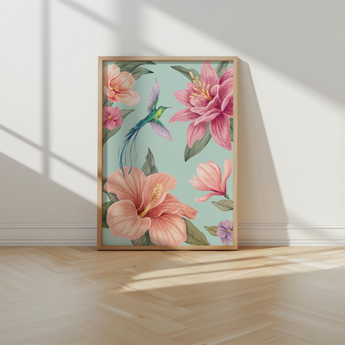 Framed floral artwork with pink flowers and a hummingbird on an aqua blue background, placed on a wooden floor.